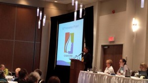 Cheryl Hayles, VP International Relations, reporting this morning on the 100th Anniversary project. Behind her we can see the 100th anniversary logo that is being used in all promotion. A beautiful pin in two sizes is available for sale from National Office.